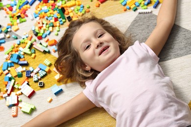 Photo of Cute girl lying near building blocks on carpet at home