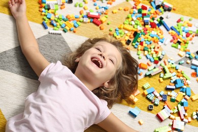 Photo of Cute girl lying near building blocks on carpet at home