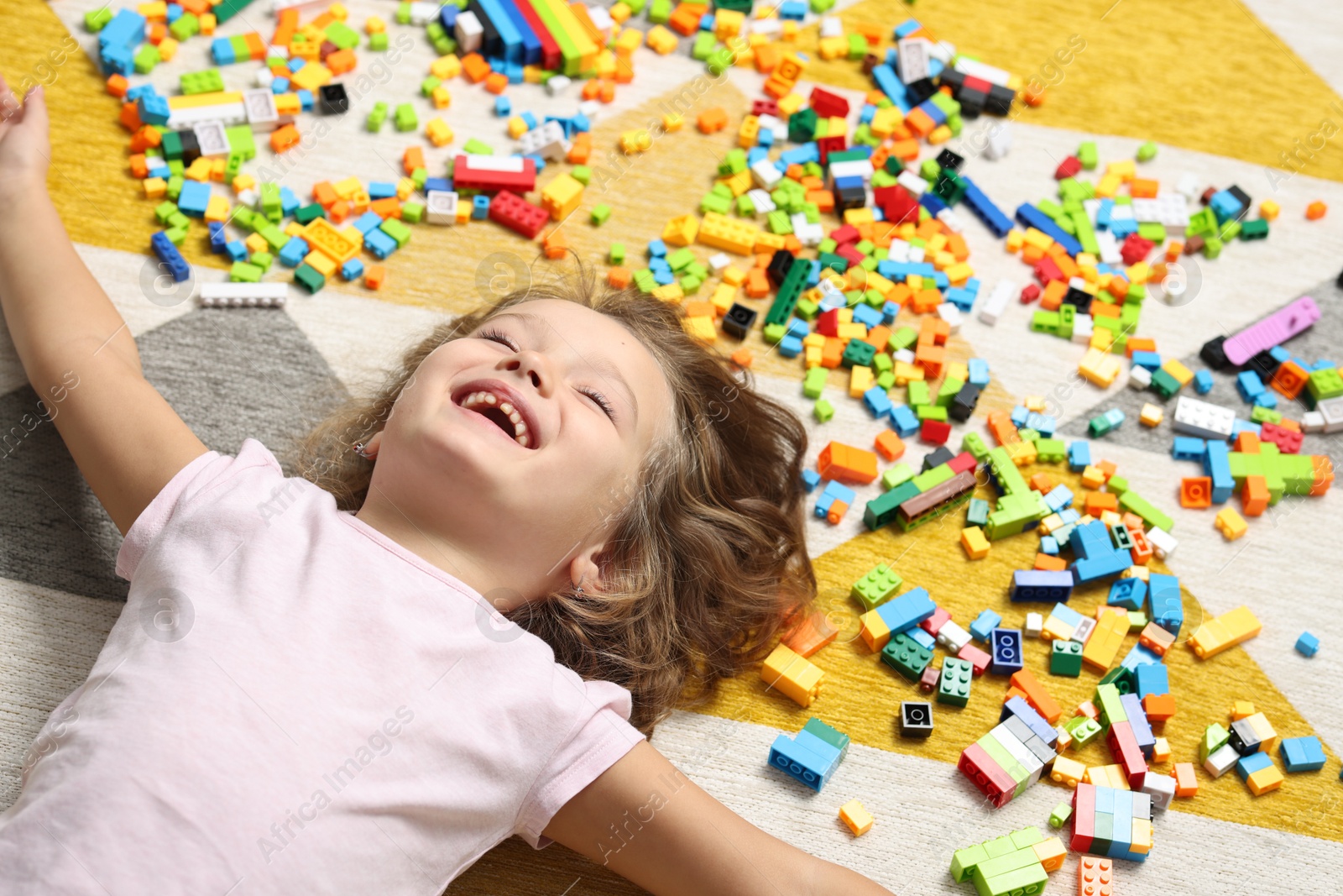 Photo of Cute girl lying near building blocks on carpet at home