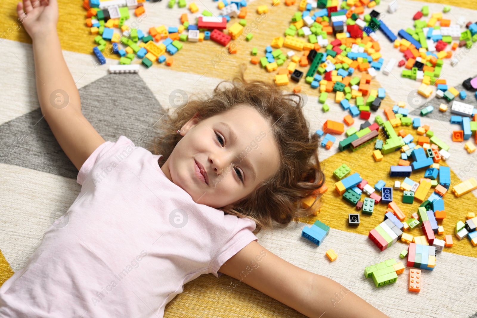 Photo of Cute girl lying near building blocks on carpet at home