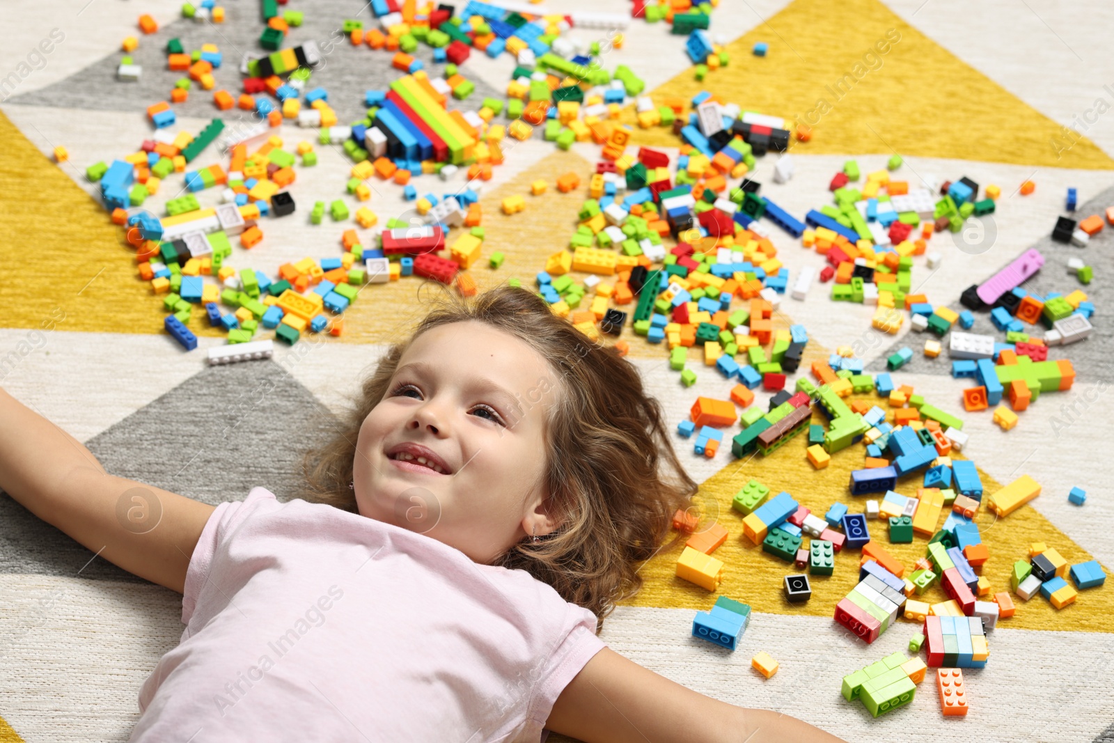 Photo of Cute girl lying near building blocks on carpet at home