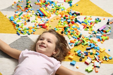 Photo of Cute girl lying near building blocks on carpet at home