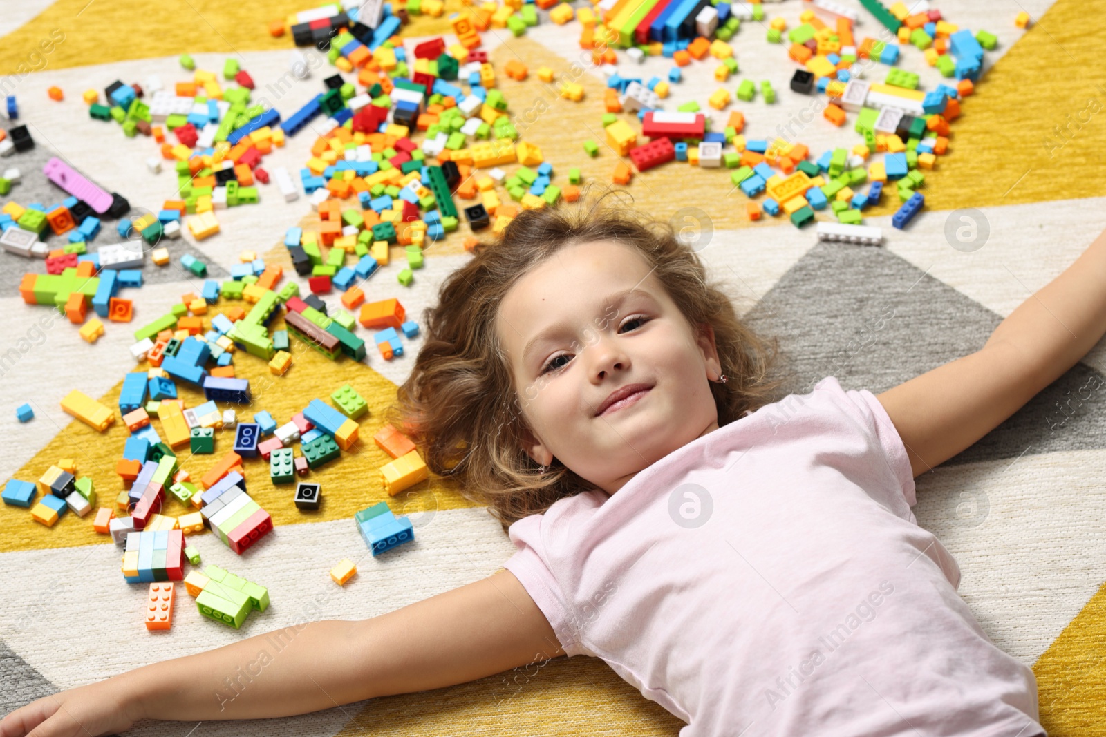 Photo of Cute girl lying near building blocks on carpet at home