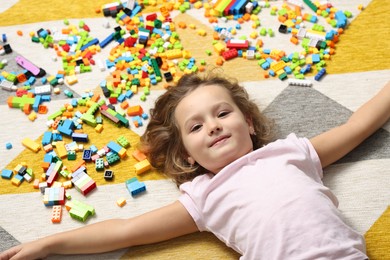 Photo of Cute girl lying near building blocks on carpet at home