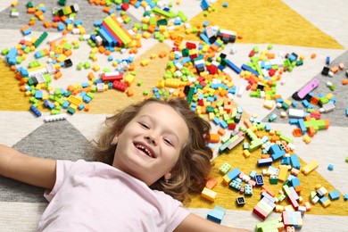 Photo of Cute girl lying near building blocks on carpet at home