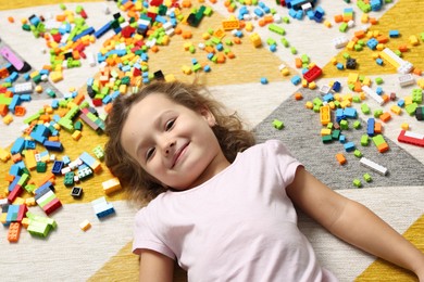 Photo of Cute girl lying near building blocks on carpet at home