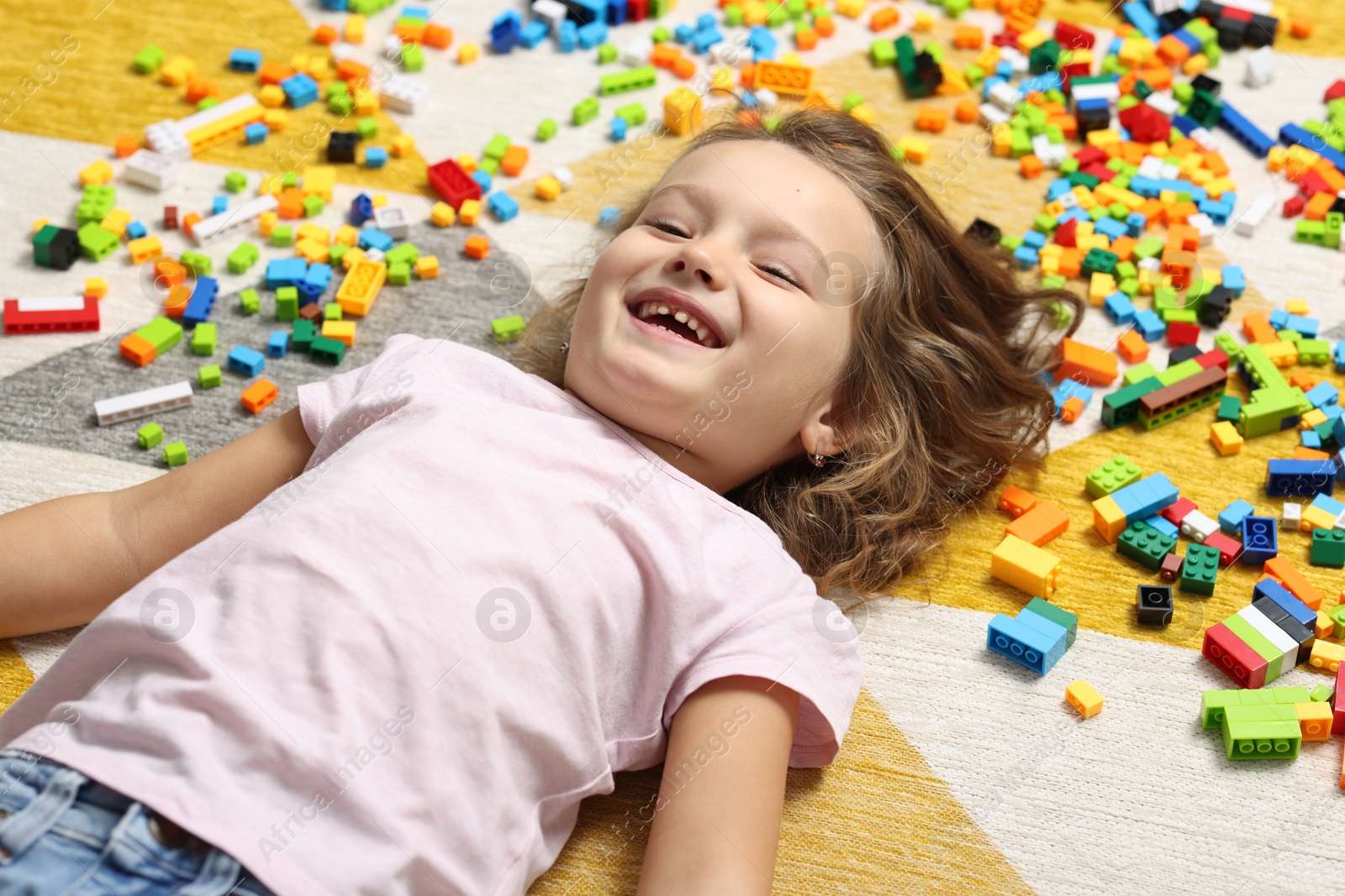 Photo of Cute girl lying near building blocks on carpet at home