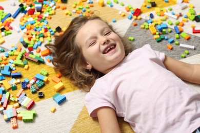 Photo of Cute girl lying near building blocks on carpet at home