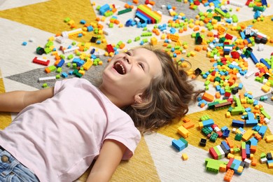 Photo of Cute girl lying near building blocks on carpet at home