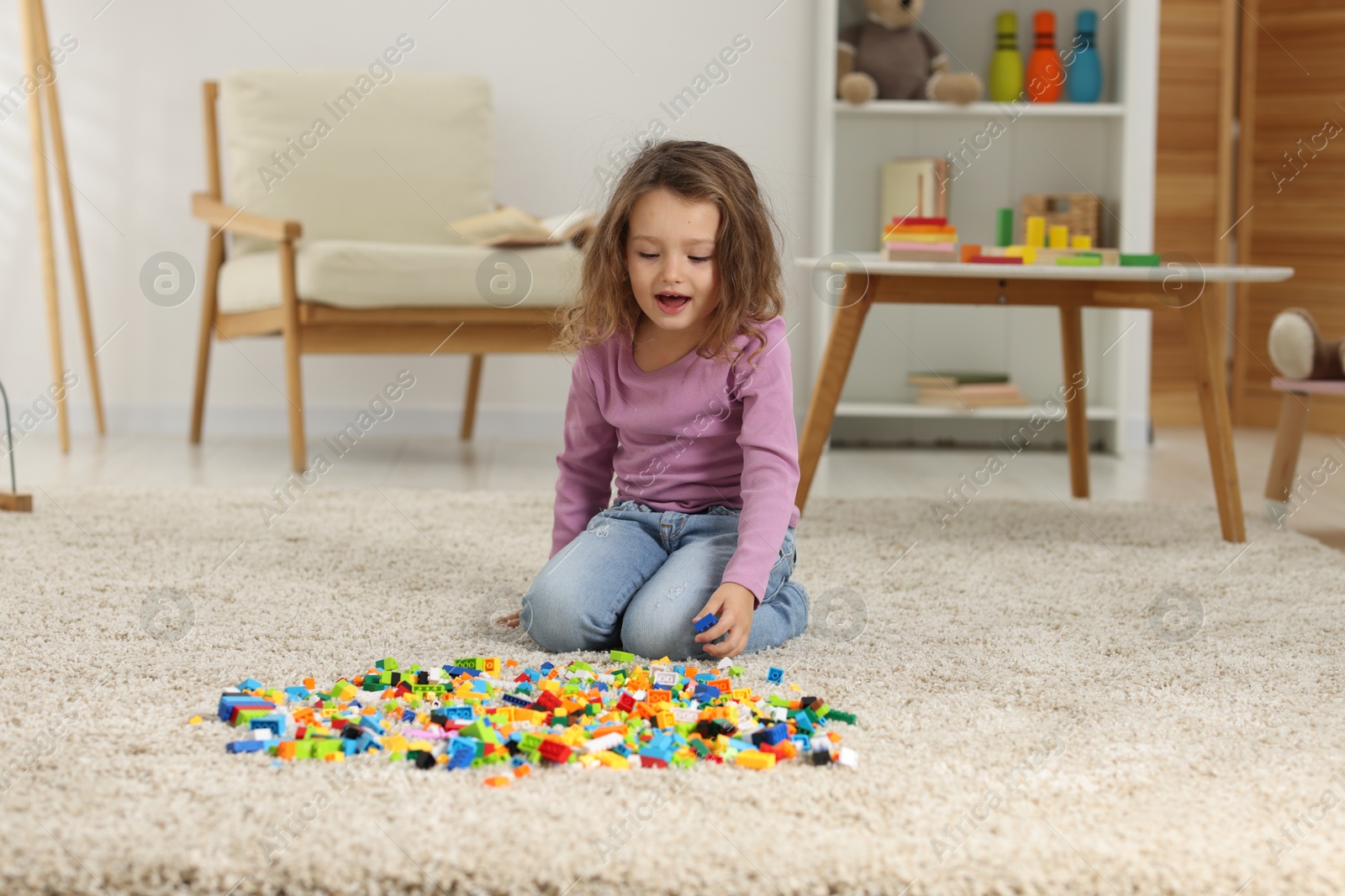 Photo of Cute girl playing with building blocks on floor at home