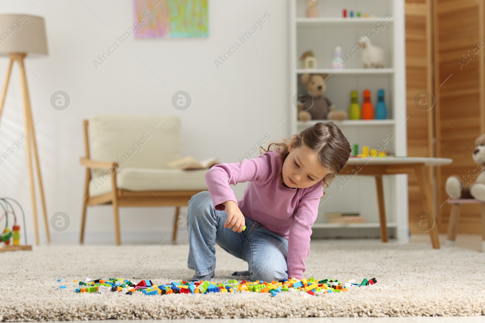 Photo of Cute girl playing with building blocks on floor at home