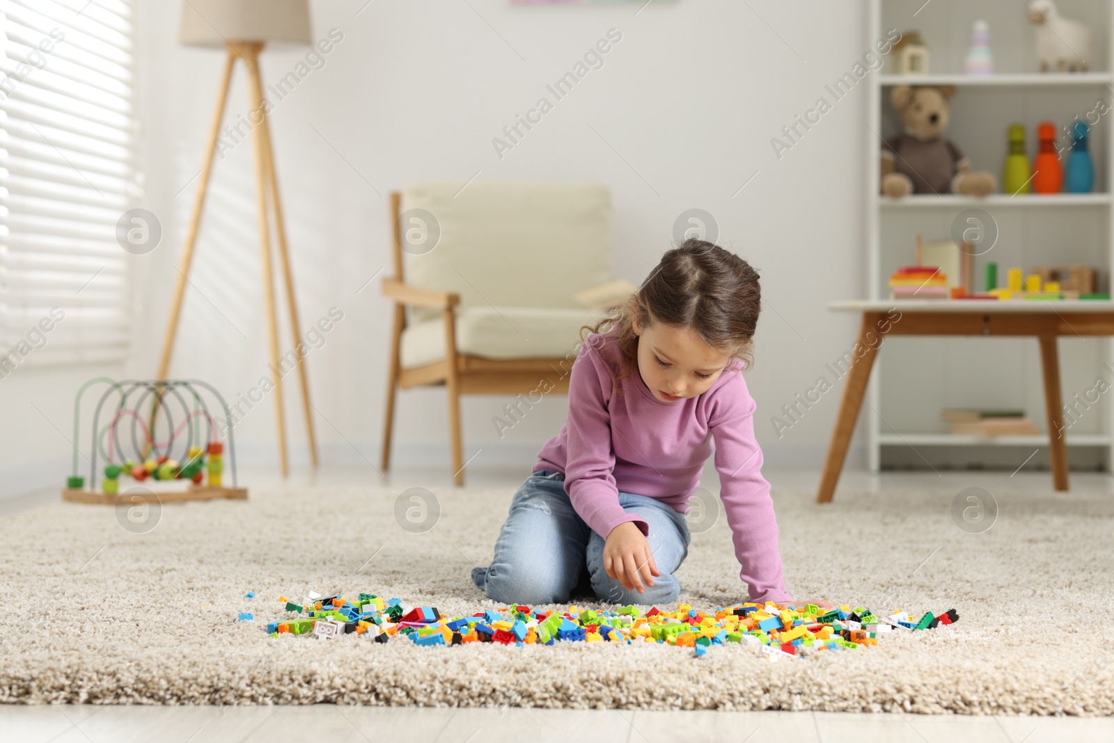 Photo of Cute girl playing with building blocks on floor at home