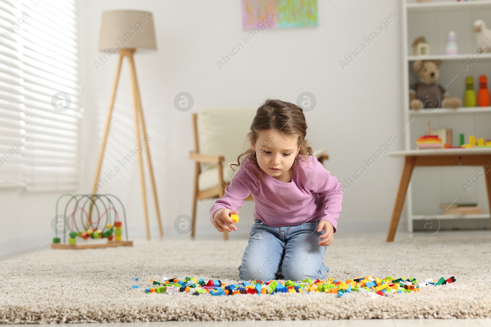 Photo of Cute girl playing with building blocks on floor at home