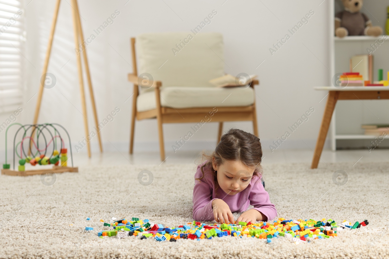 Photo of Cute girl playing with building blocks on floor at home