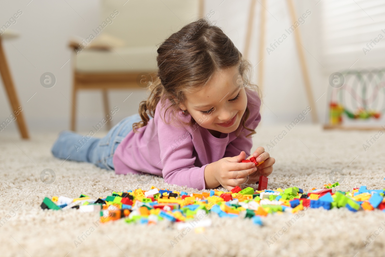 Photo of Cute girl playing with building blocks on floor at home