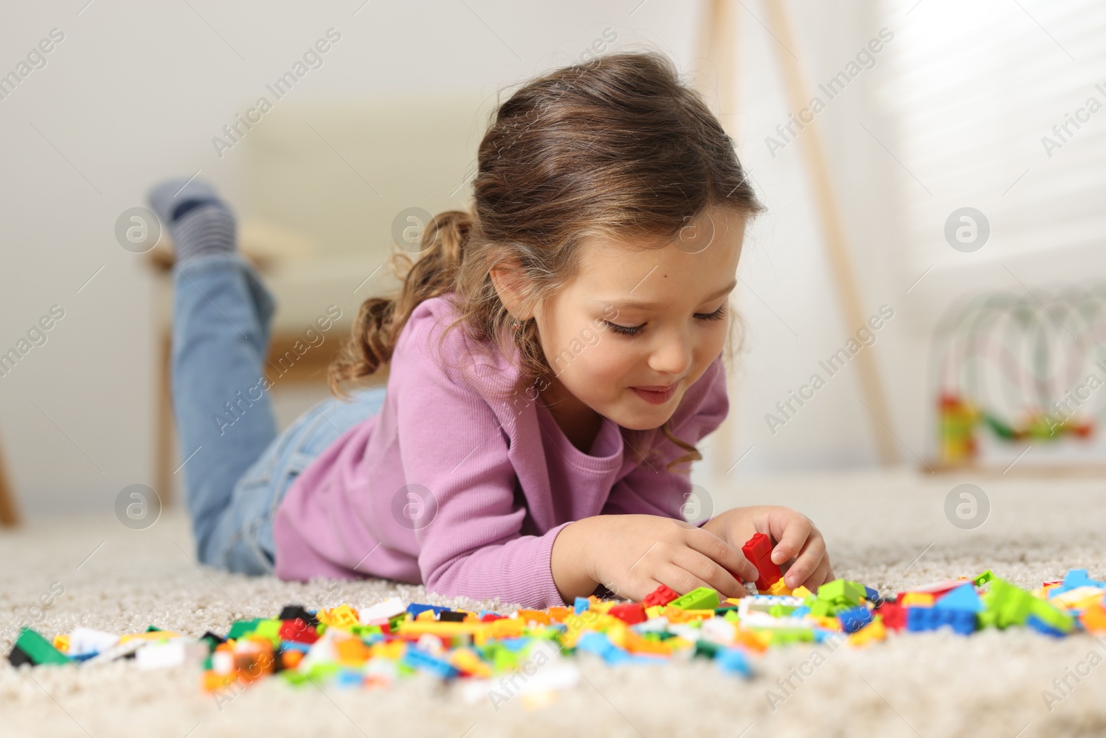 Photo of Cute girl playing with building blocks on floor at home