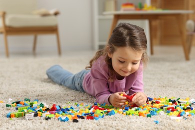 Photo of Cute girl playing with building blocks on floor at home