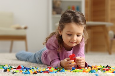 Photo of Cute girl playing with building blocks on floor at home