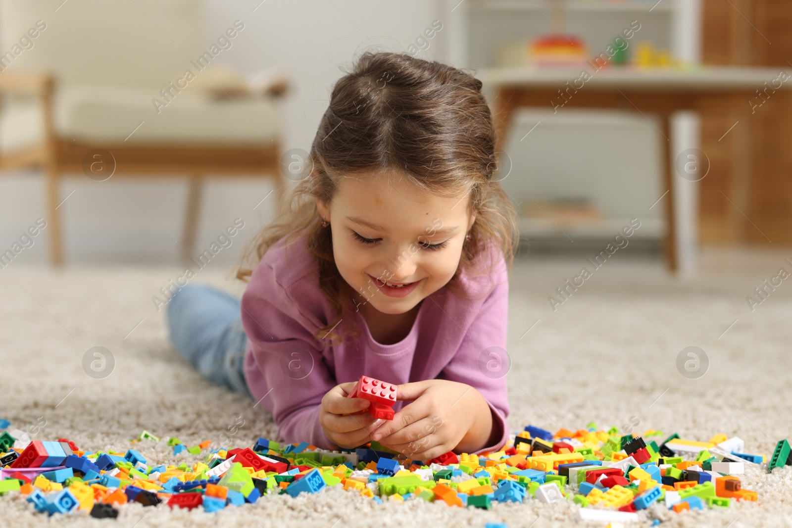 Photo of Cute girl playing with building blocks on floor at home