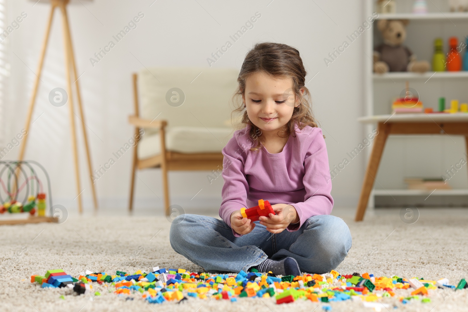 Photo of Cute girl playing with building blocks on floor at home