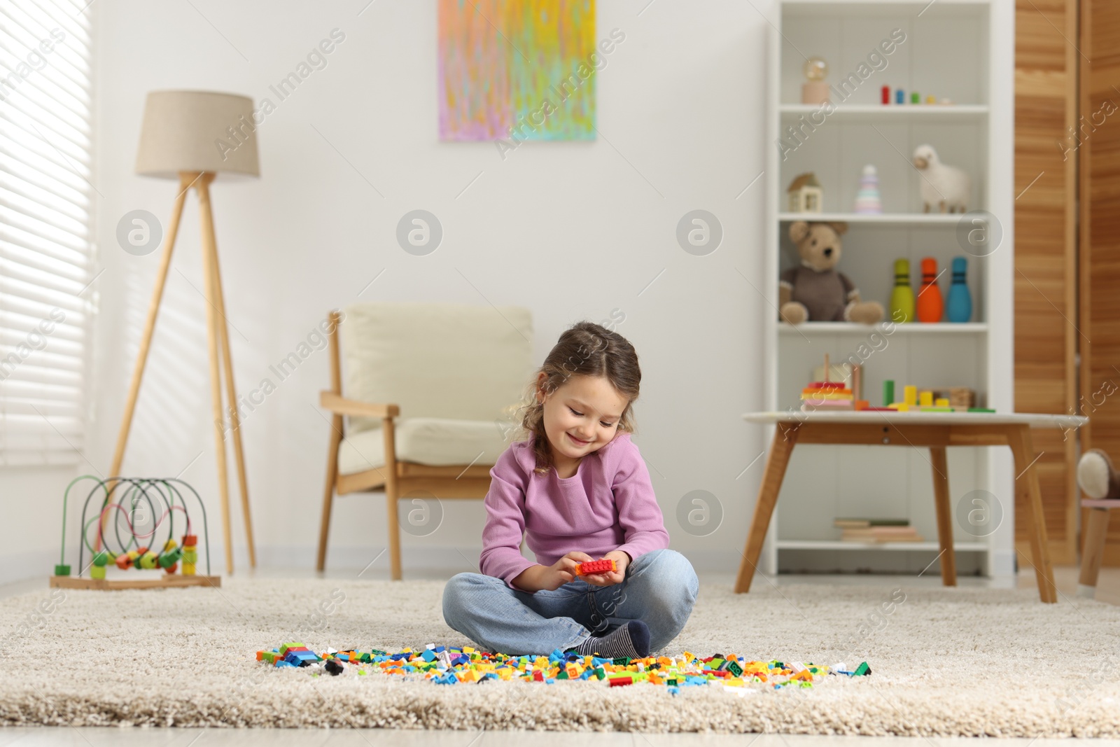 Photo of Cute girl playing with building blocks on floor at home