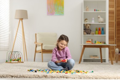 Photo of Cute girl playing with building blocks on floor at home