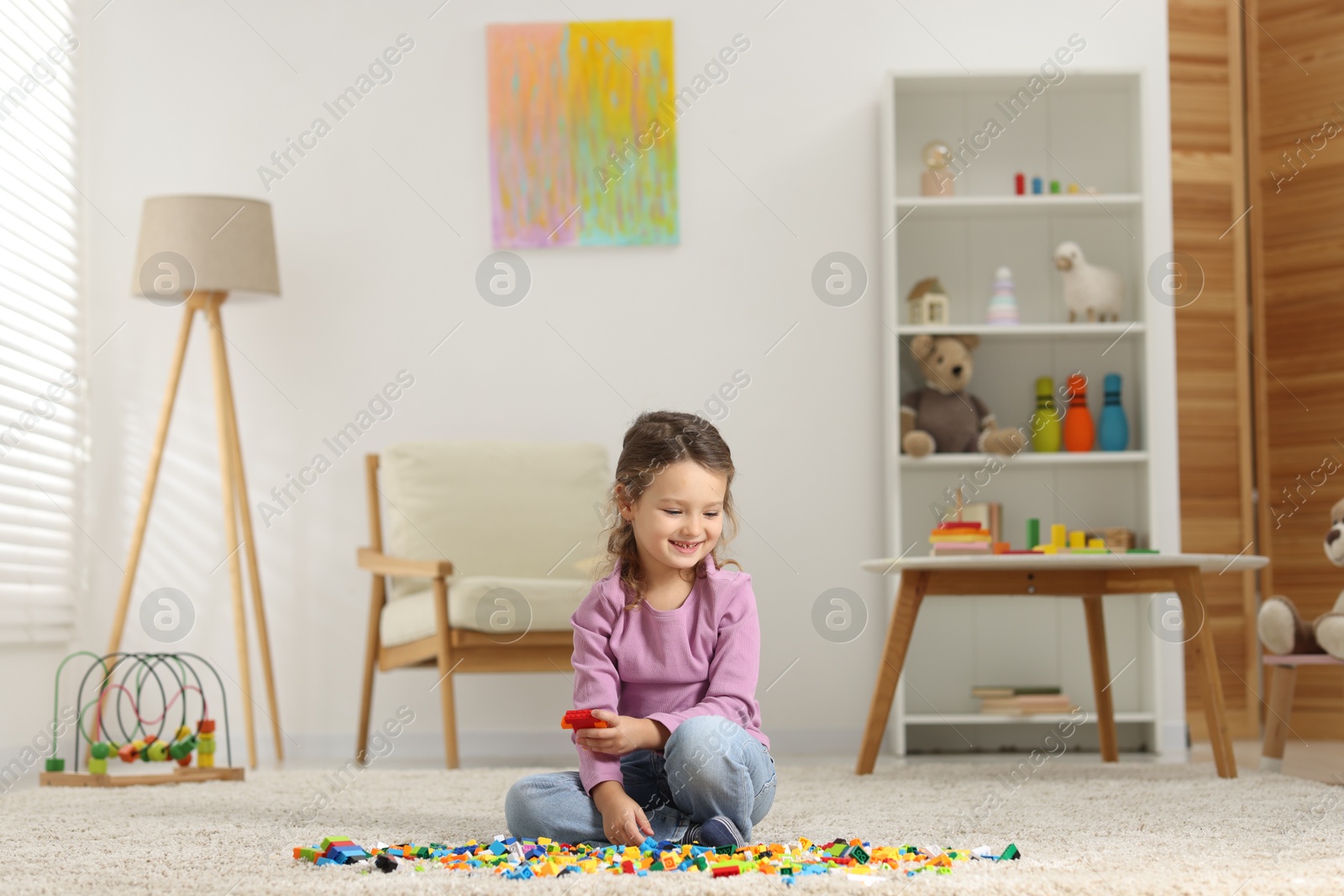 Photo of Cute girl playing with building blocks on floor at home