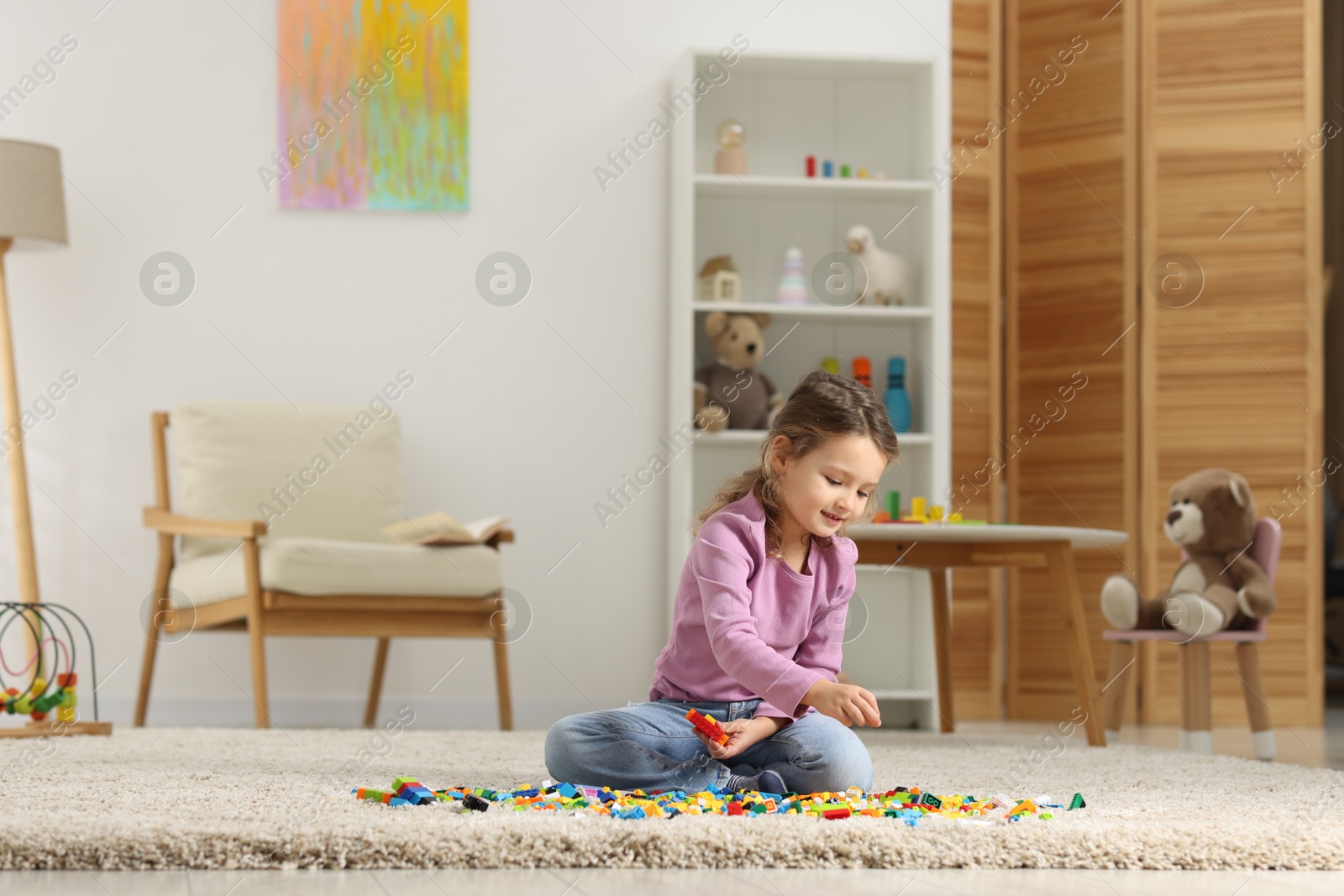 Photo of Cute girl playing with building blocks on floor at home. Space for text