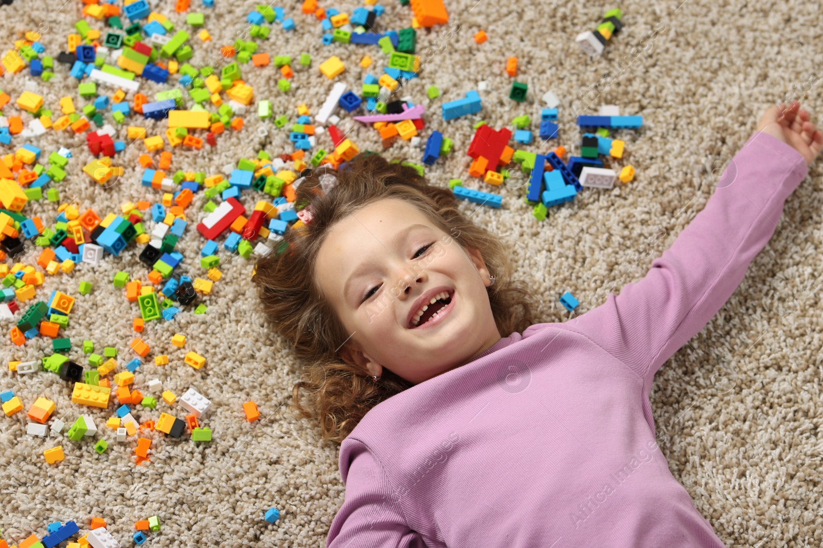 Photo of Cute girl lying near building blocks on carpet at home