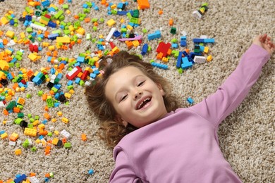 Photo of Cute girl lying near building blocks on carpet at home