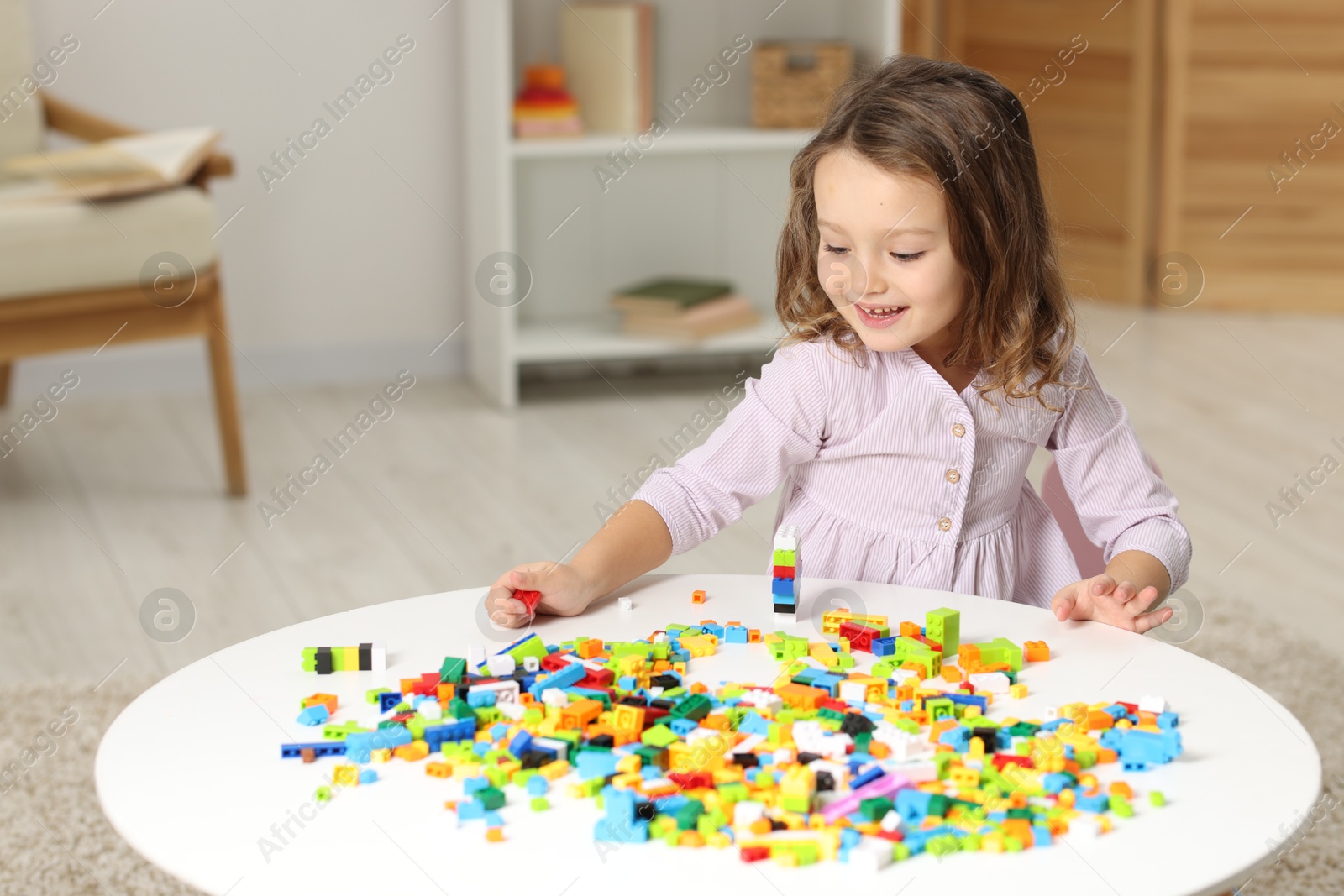 Photo of Cute girl playing with building blocks at white table indoors. Space for text