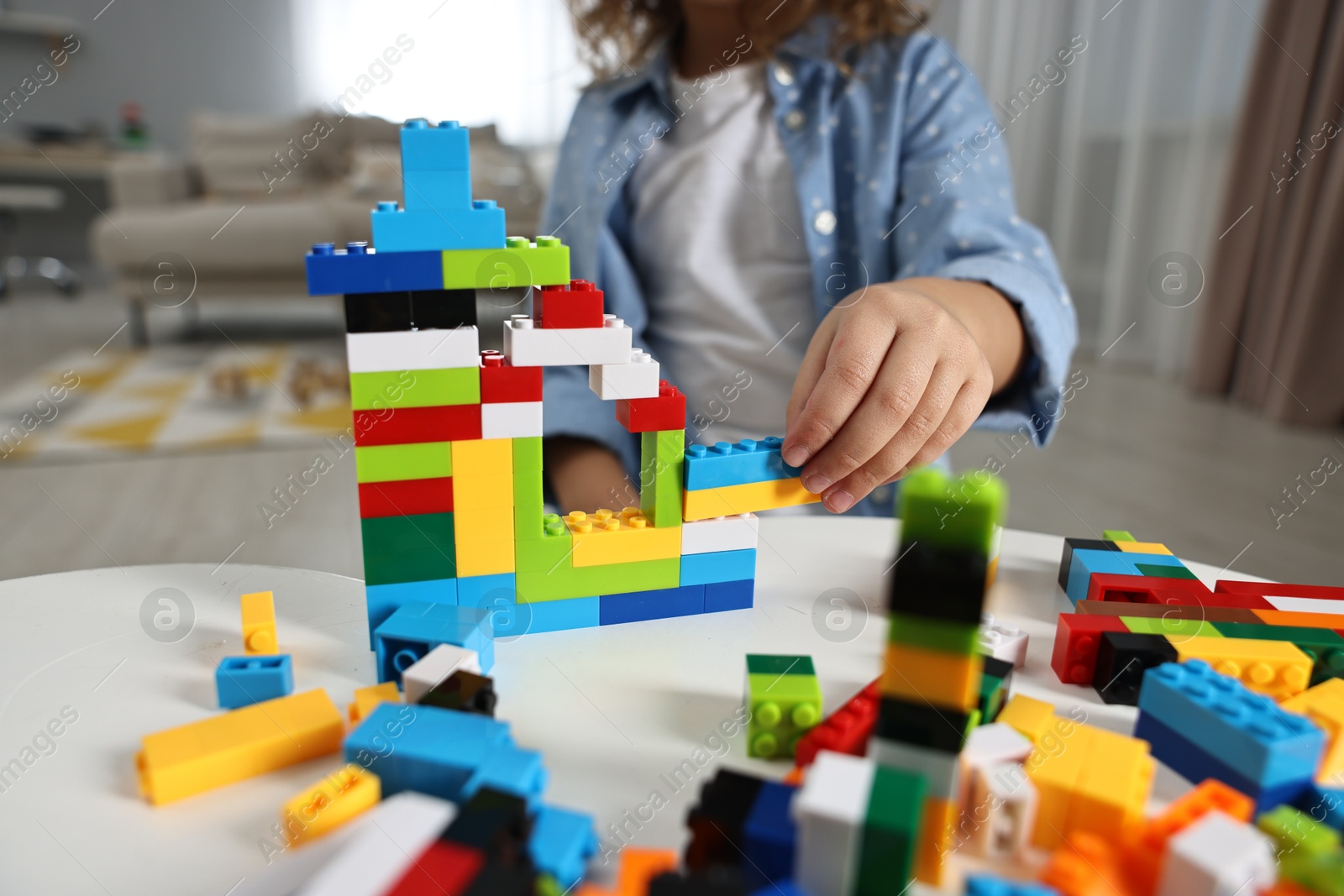 Photo of Girl playing with building blocks at white table indoors, closeup. Selective focus