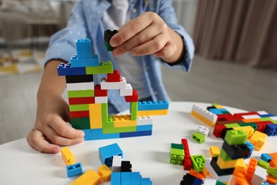 Photo of Girl playing with building blocks at white table indoors, closeup. Selective focus