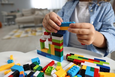 Photo of Girl playing with building blocks at white table indoors, closeup. Selective focus