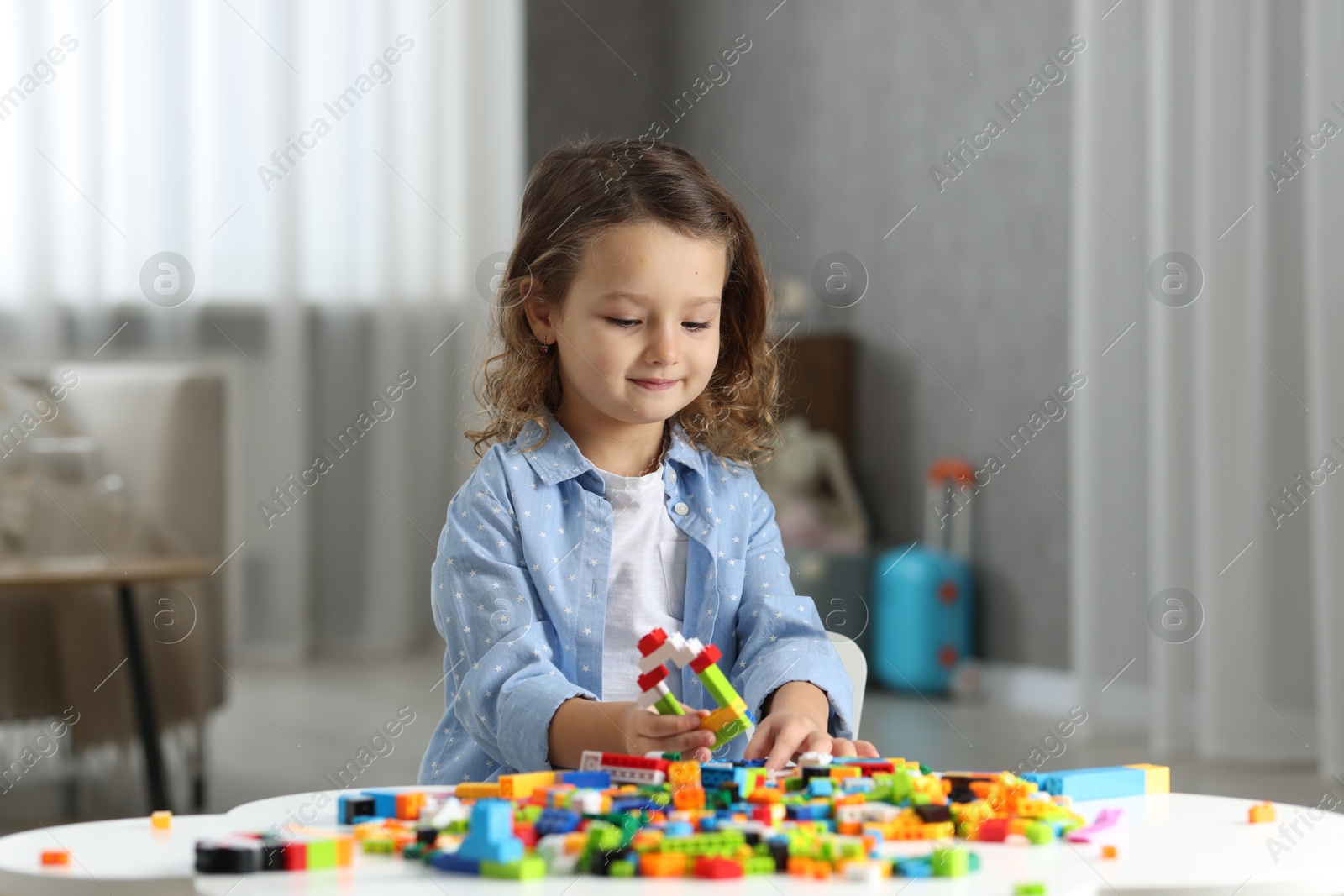 Photo of Cute girl playing with building blocks at white table indoors