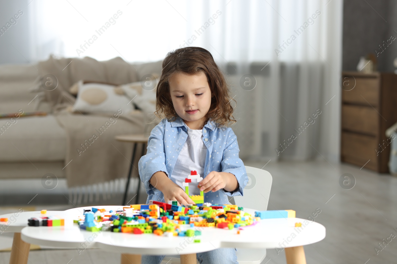 Photo of Cute girl playing with building blocks at white table indoors