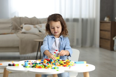 Photo of Cute girl playing with building blocks at white table indoors