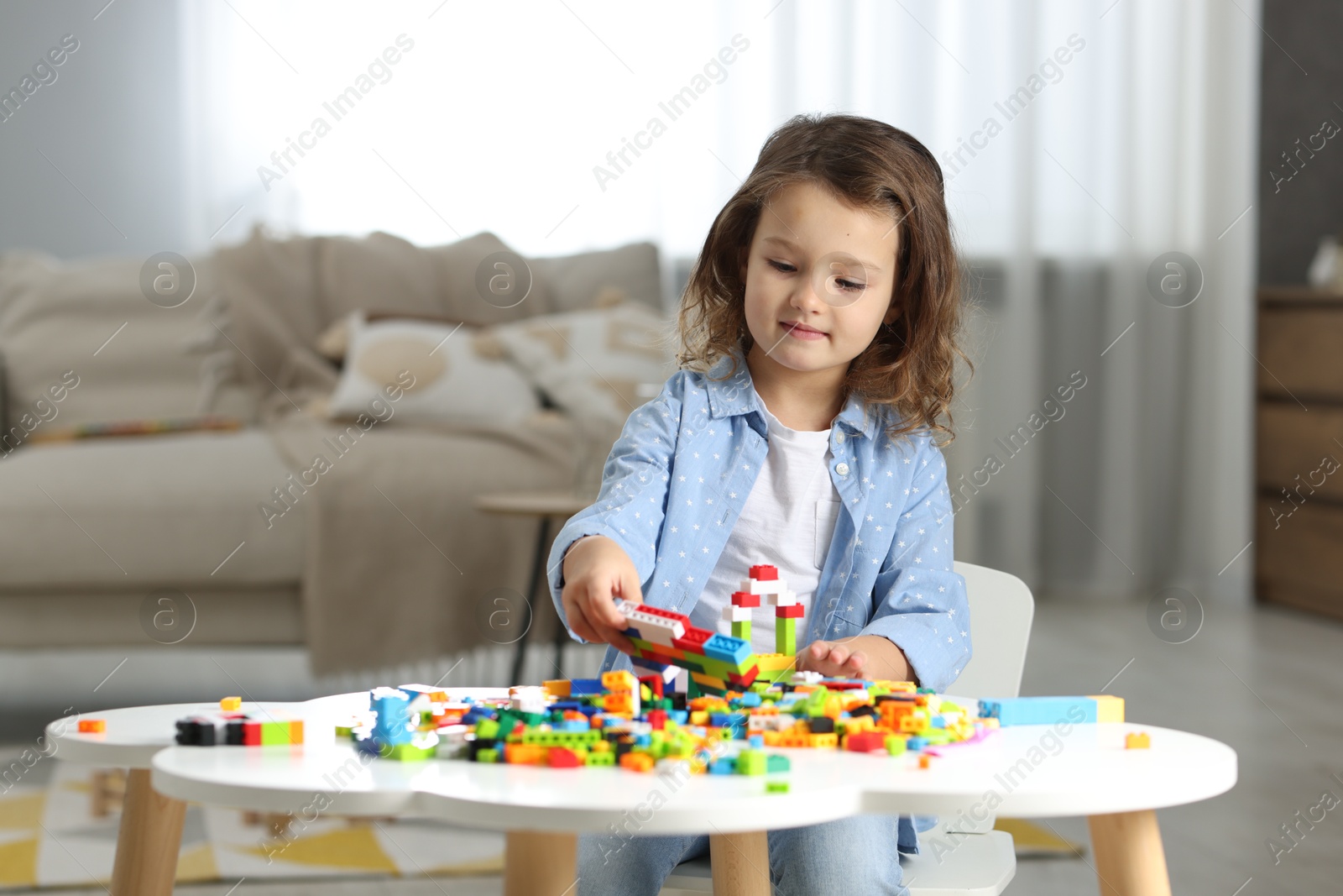 Photo of Cute girl playing with building blocks at white table indoors