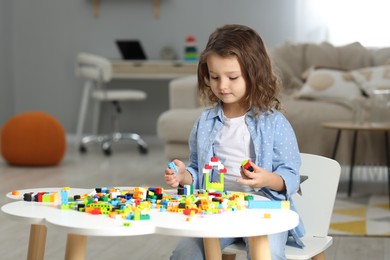 Photo of Cute girl playing with building blocks at white table indoors