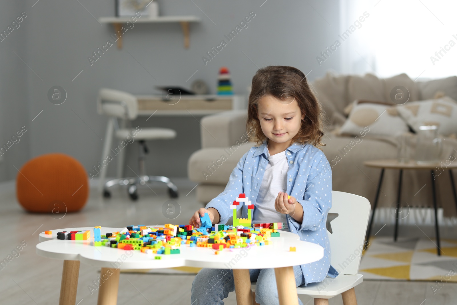 Photo of Cute girl playing with building blocks at white table indoors