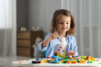 Photo of Cute girl playing with building blocks at white table indoors