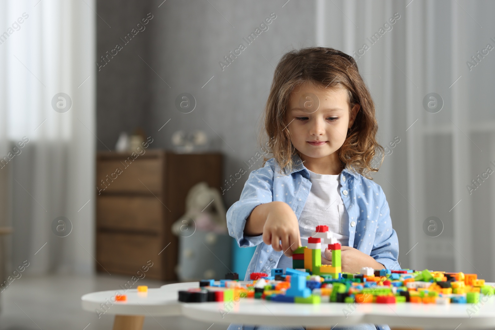 Photo of Cute girl playing with building blocks at white table indoors