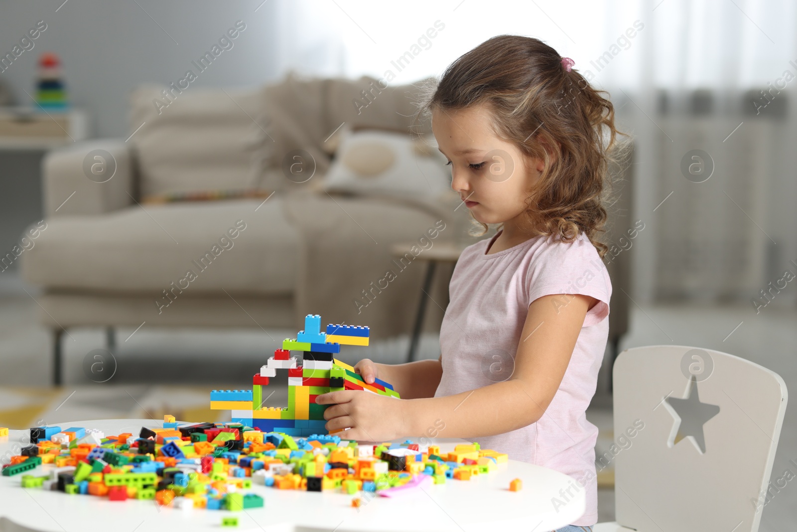 Photo of Cute girl playing with building blocks at white table indoors