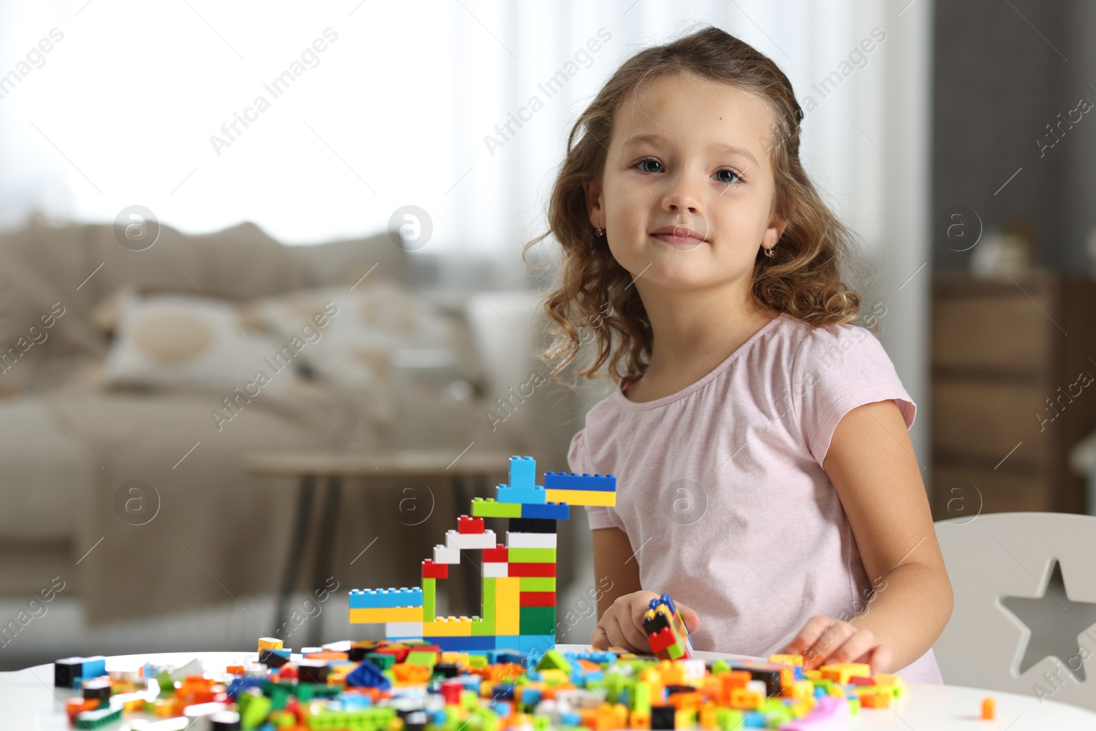 Photo of Cute girl playing with building blocks at white table indoors