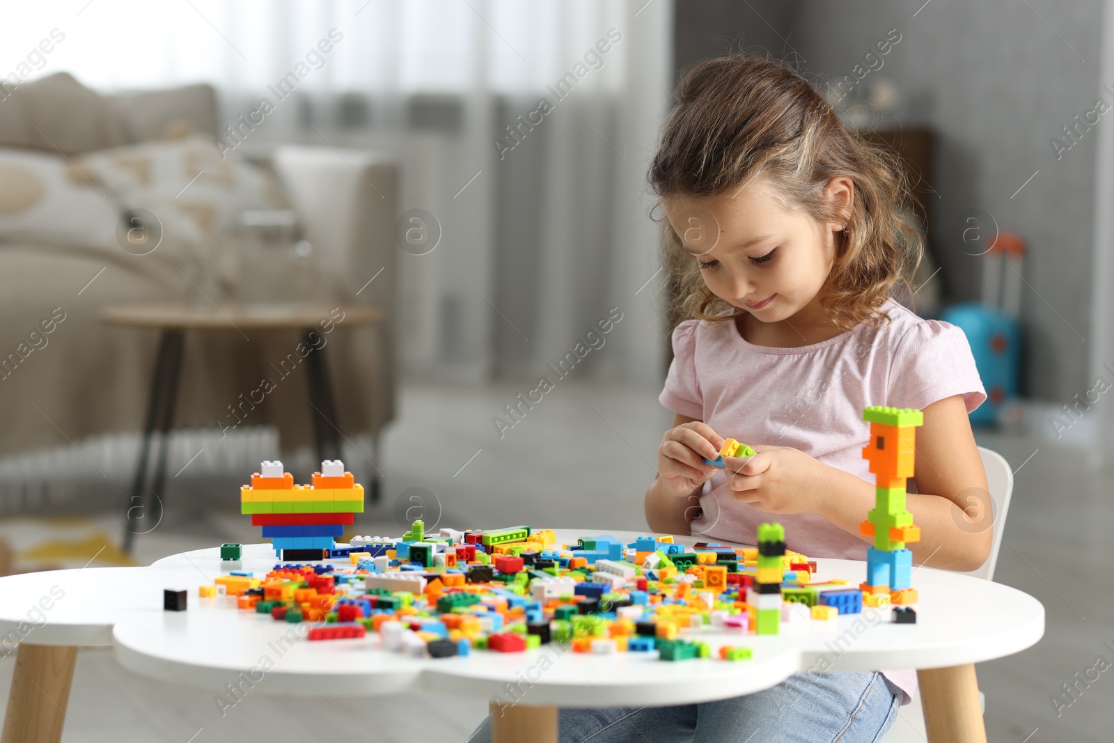 Photo of Cute girl playing with building blocks at white table indoors. Space for text