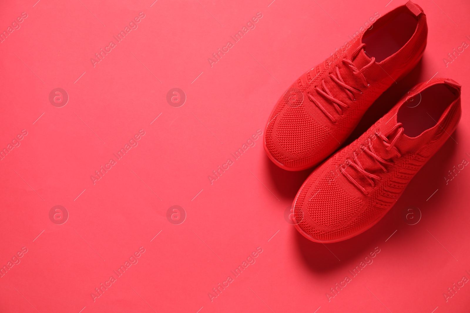 Photo of Sportive shoes. Pair of stylish sneakers on crimson background, flat lay. Space for text