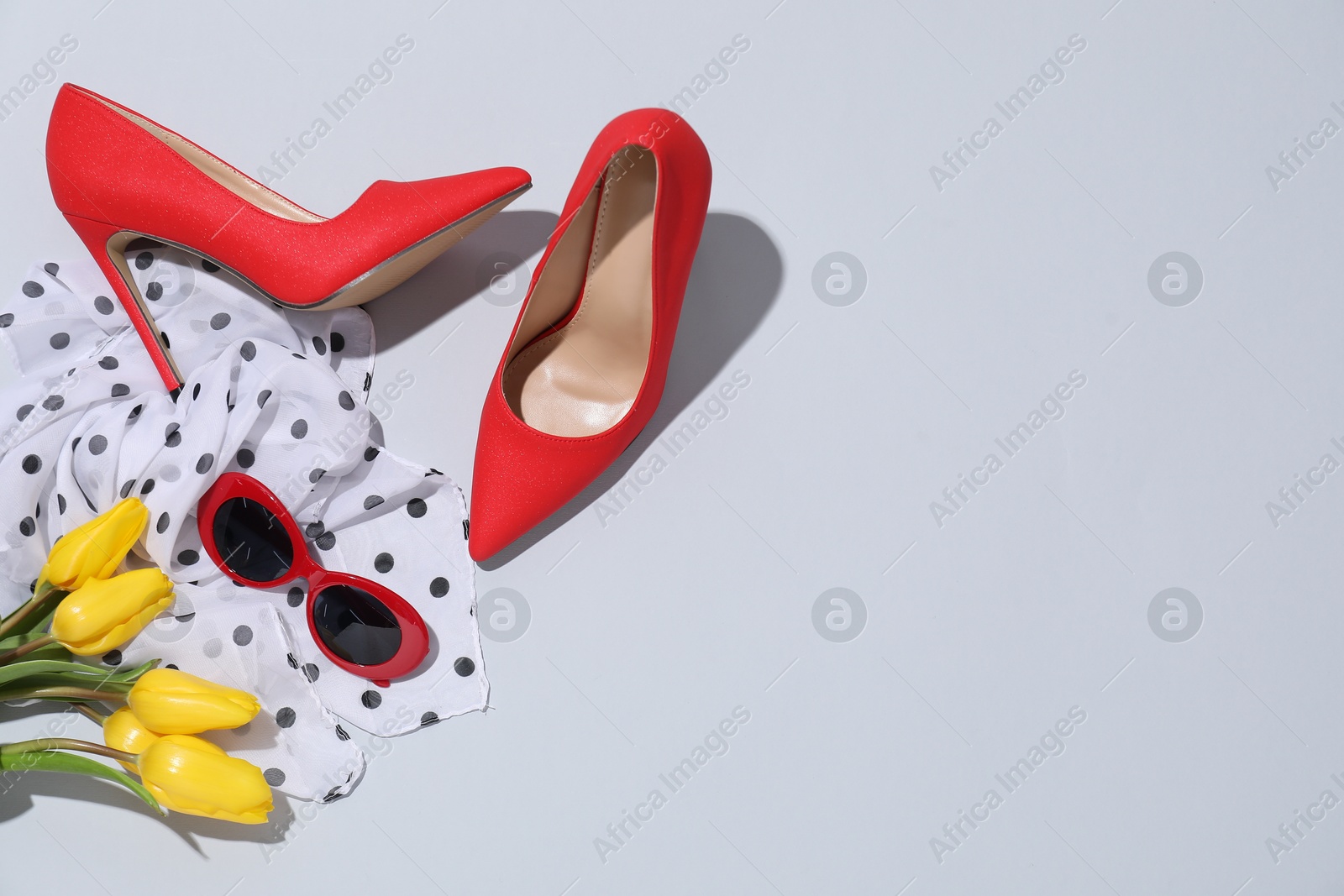 Photo of Red high heeled shoes, scarf, tulips and sunglasses on light background, flat lay. Space for text