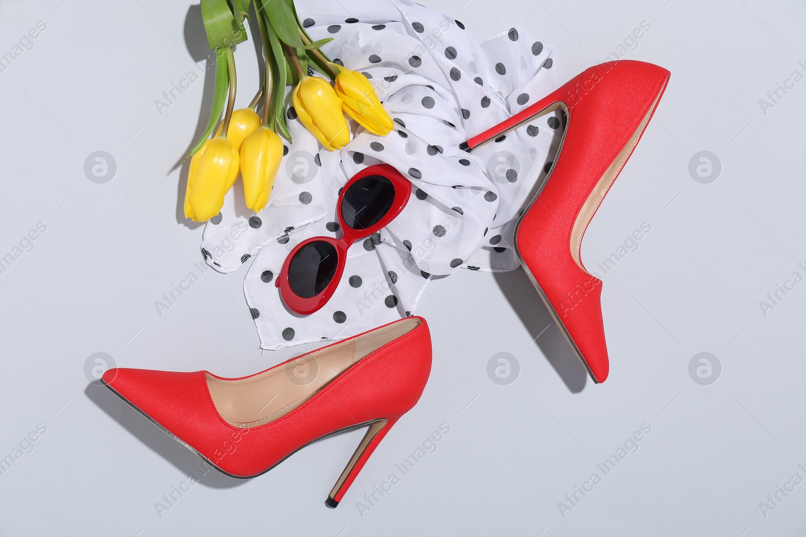 Photo of Red high heeled shoes, scarf, tulips and sunglasses on light background, flat lay