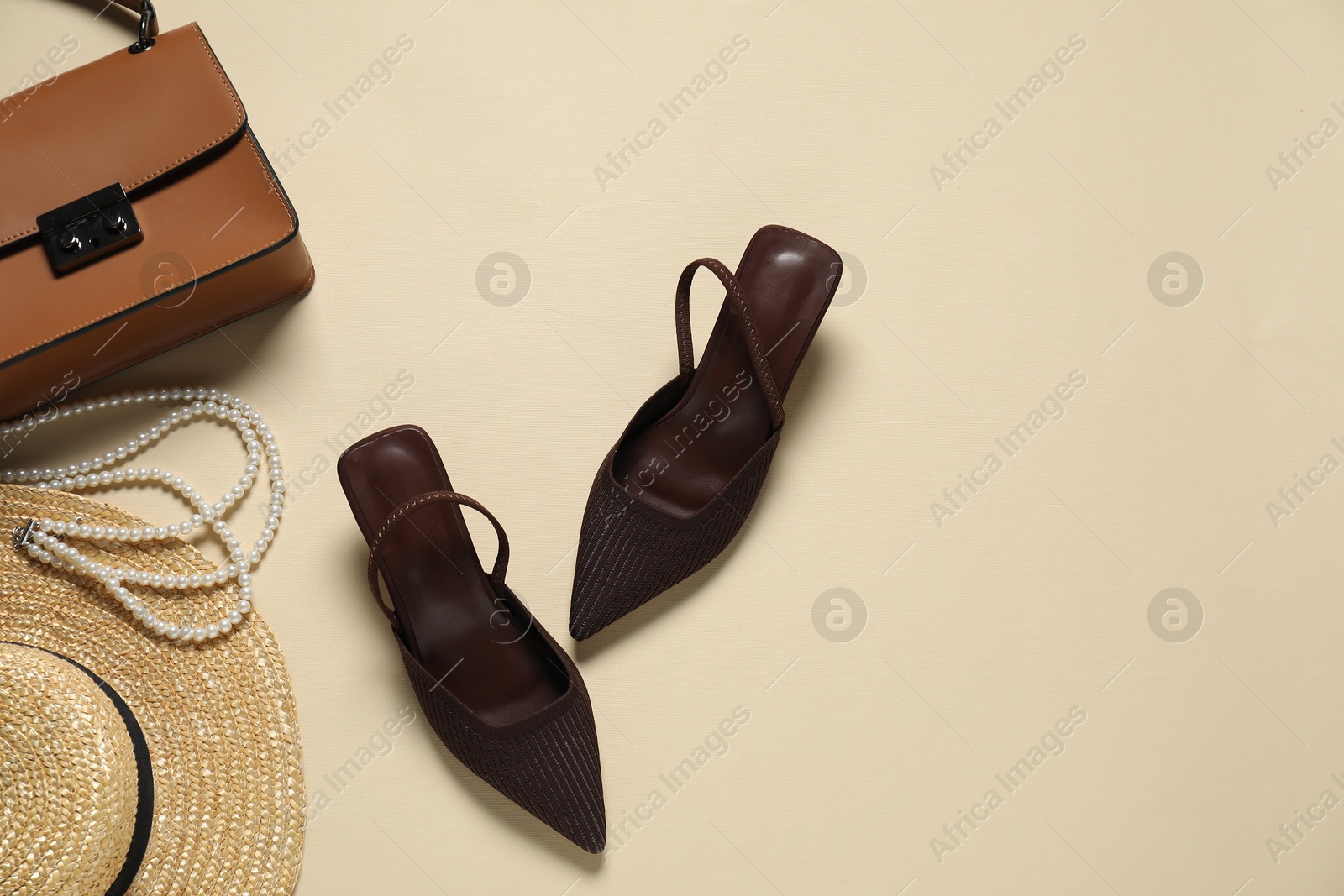 Photo of Stylish brown shoes, straw hat, bag and pearl necklace on beige background, flat lay. Space for text