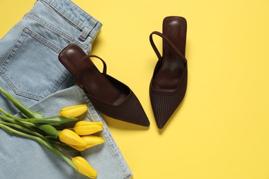 Photo of Stylish brown shoes, jeans and tulips on yellow background, flat lay